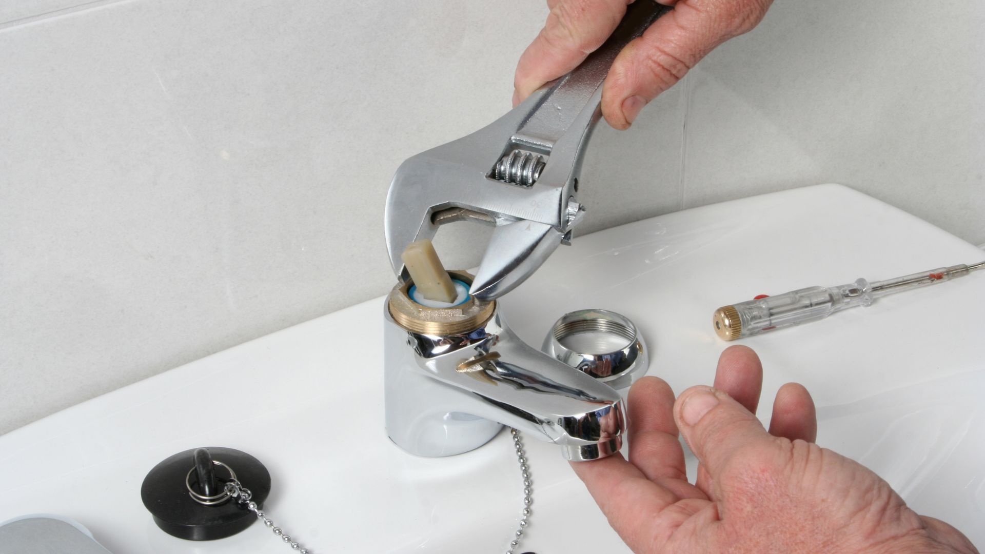 A man fixing a sink faucet with a wrench